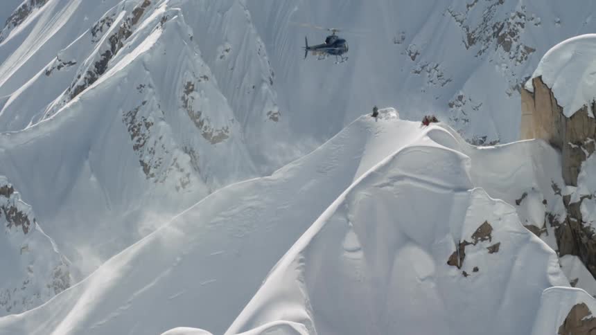 A helicopter hovers over a mountain slope covered in snow