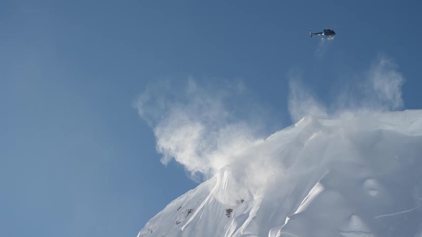 A helicopter is flying above a snow covered mountain