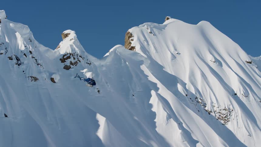 Helicopter flies along snow covered mountain slope before turning