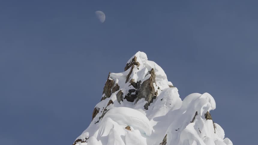 Moon above snowy mountain peak during daytime