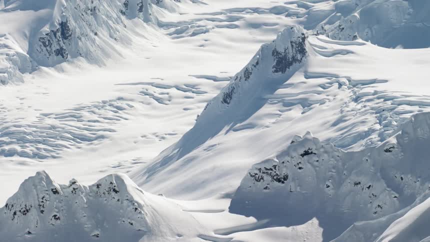 The slope of a steep mountain is covered in snow drifts