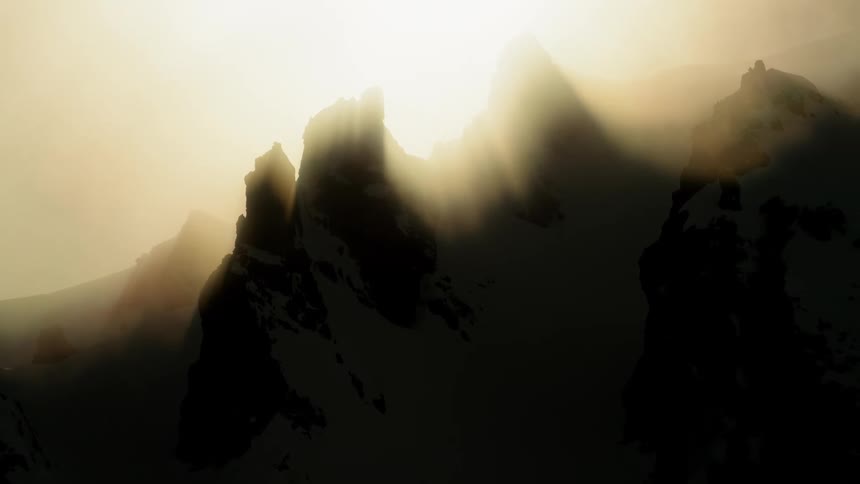 The sun glares over a snow covered rocky and jagged mountain ridge