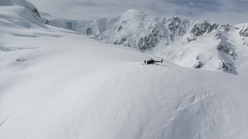 People are standing around the helicopter on the mountain