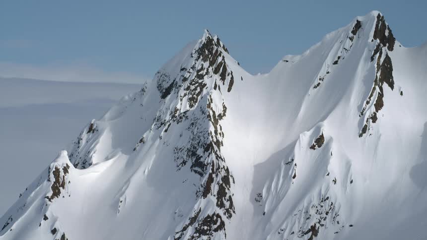 The top of a snow covered mountain ridge looming over the clouds