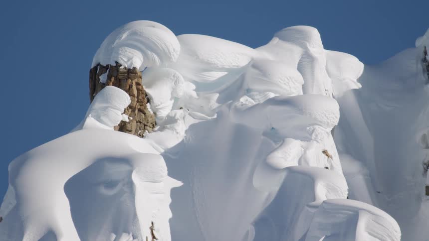 A snow covered mountain ridge against a bright blue sky comes into focus