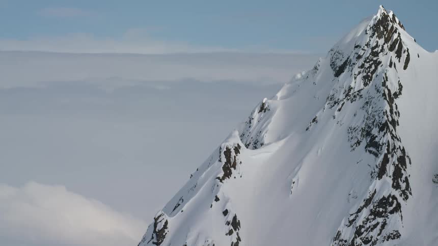 Mountain peak covered in snow and surrounded by clouds on a clear day
