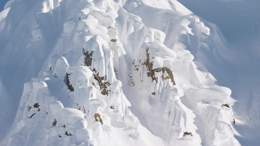 Snow covered rough slope lit by sunshine bordered by shadowy valleys