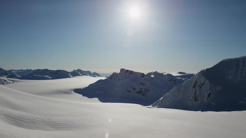 A snow covered landscape topped with mountains and a clear blue sky
