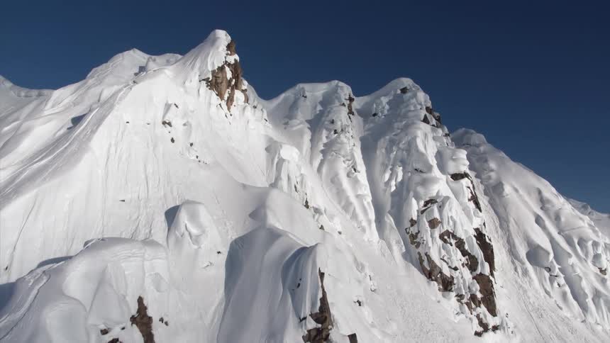 Snow covered mountain ridge with steel slopes against a dark blue sky