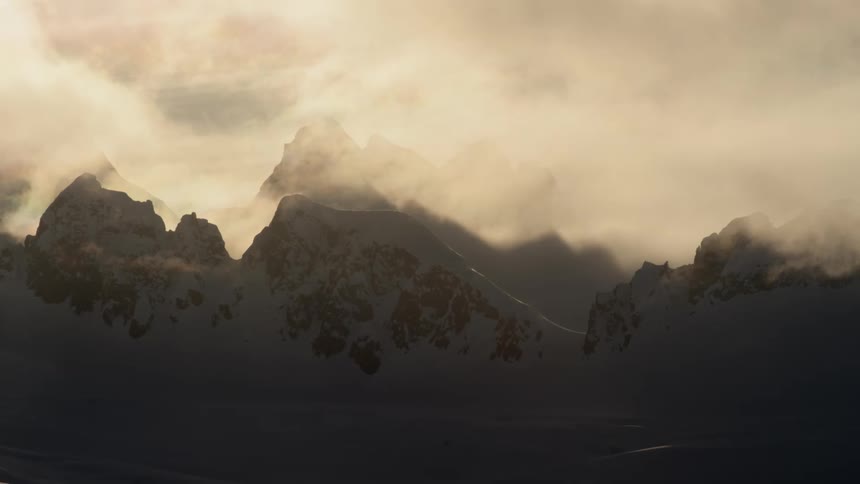 Low lying clouds shroud tops of snow covered mountains on edge of snowy plains