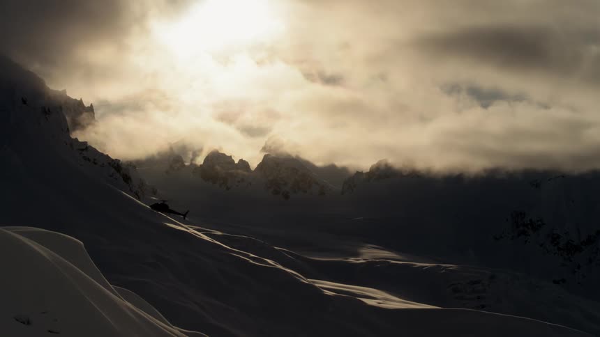 Helicopter lands on snow drift in front of rugged snow covered mountain range
