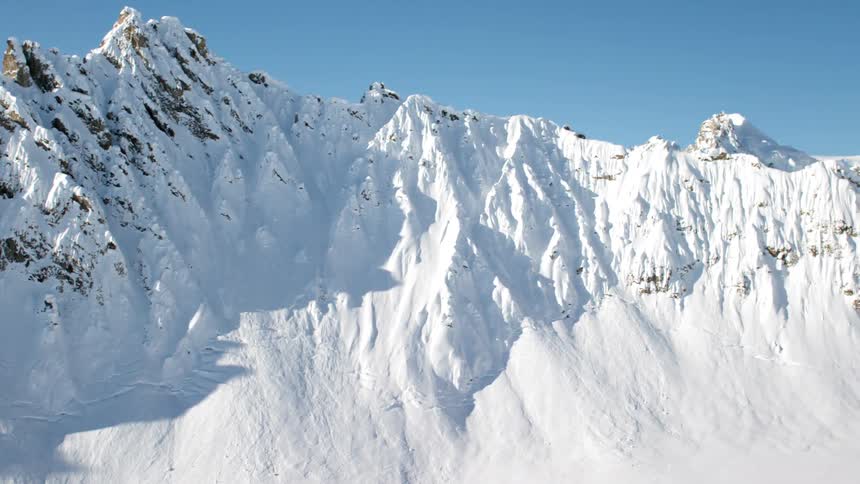 A mountain range with cliffs covered in snow and snow drifts