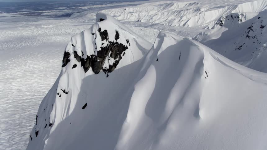 The peak of a snow covered mountain looming of an arctic tundra