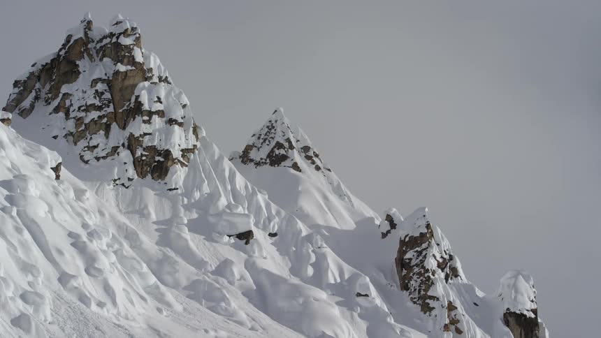 A jagged mountain ridge covered with snow with clouds hanging over head