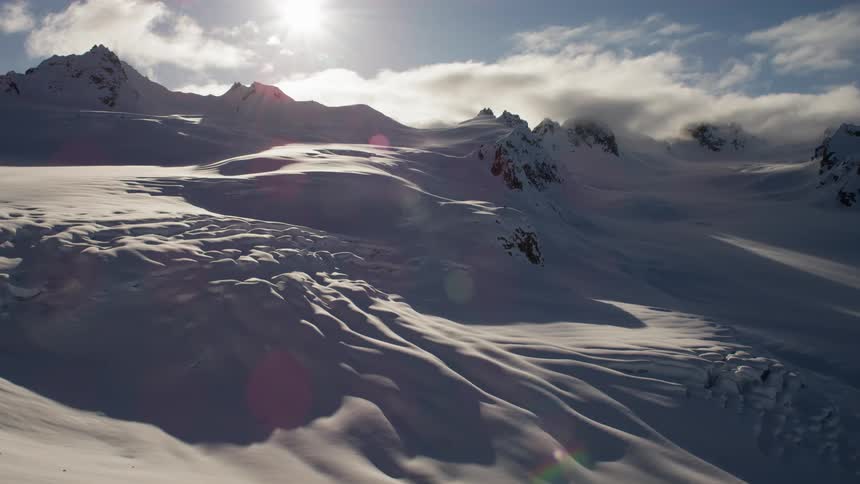 A snow covered mountain range with the sky and the sun in the background