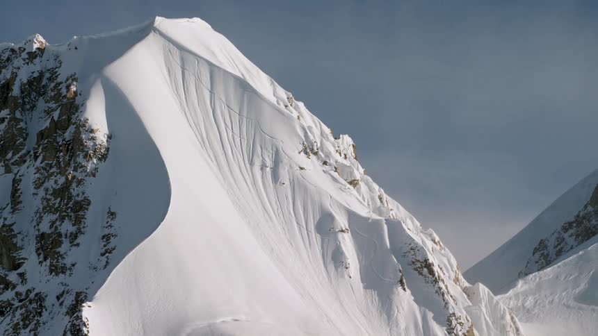 Snow covers mountain slopes under lightly cloudy sky
