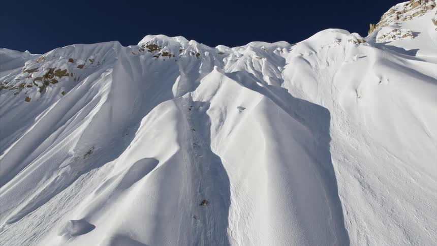 A rocky mountain slope covered in dunes of snow