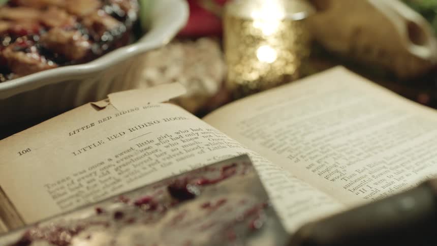 A book and a bowl of food sit on a table along with a burning candle