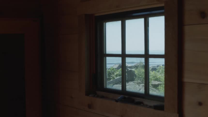 A wood paneled wall with a window looks out to a body of water