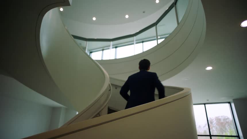 Man in suit walks up spiral staircase