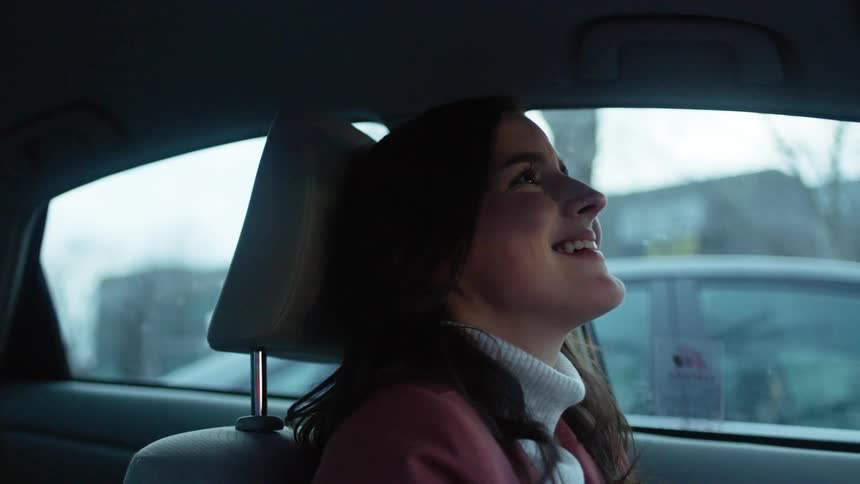 A woman is sitting her car laughing and puts both hands over her face