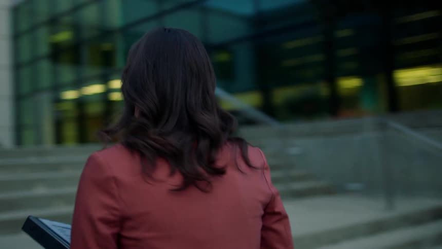 A woman carrying binders walks towards an office building