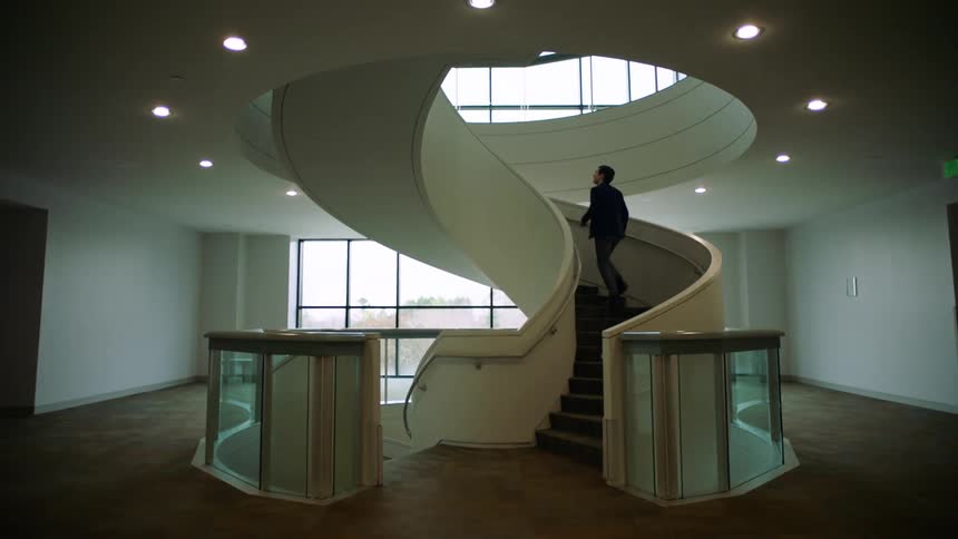 A white man in a suit climbs a staircase in an office building