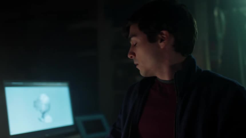 A young man in a an office looks at a laptop and writes on paper