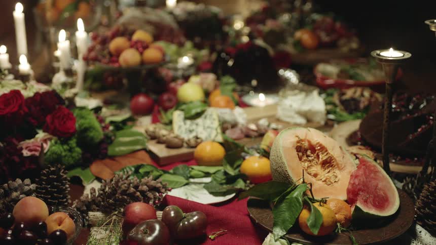 A dining table covered with piles of fruit and burning candles