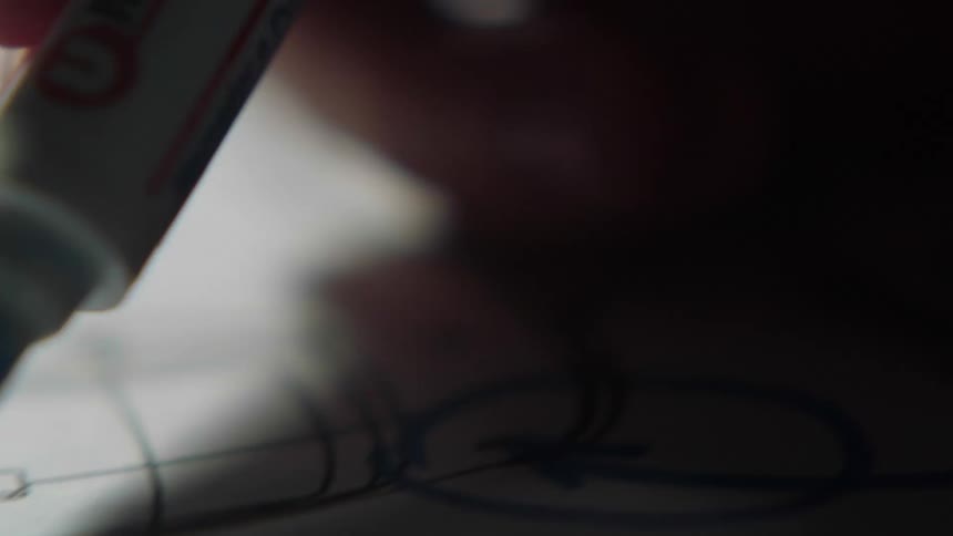 A persons hand writing on a piece of paper with a blue marker