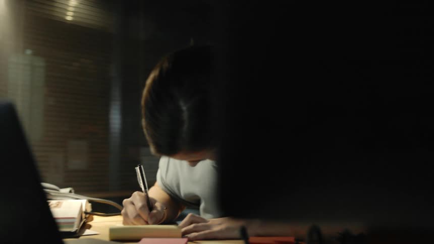 A female sitting in front of a computer writes on paper