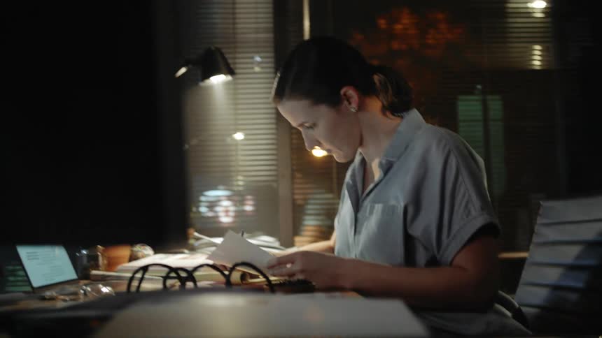 Woman sitting at desk does paperwork in dark room under lamp