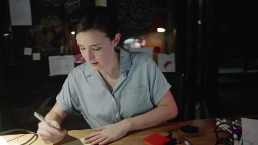A woman nods after looking at a laptop then writes a note on a pad
