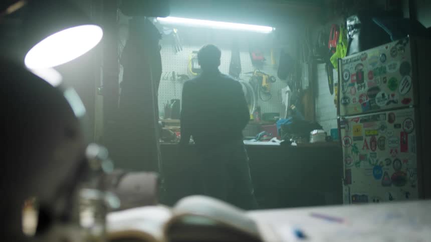 A man standing by a workbench next to a refrigerator