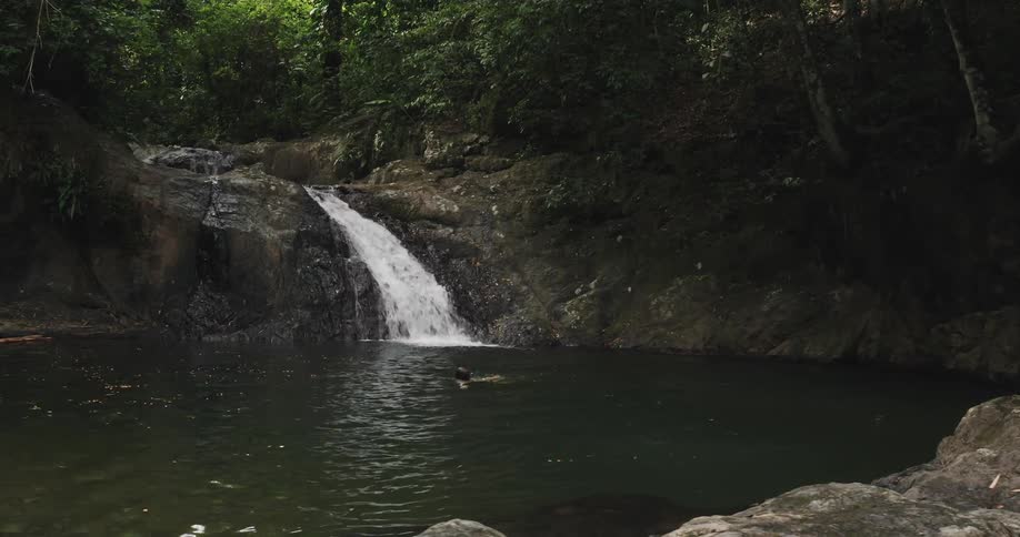 Woman swims in swimming hole fed by small waterfall