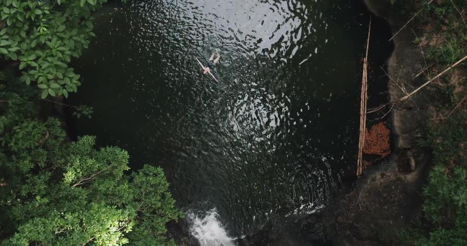 Birds eye view of woman swimming in a swimming hole with a waterfall