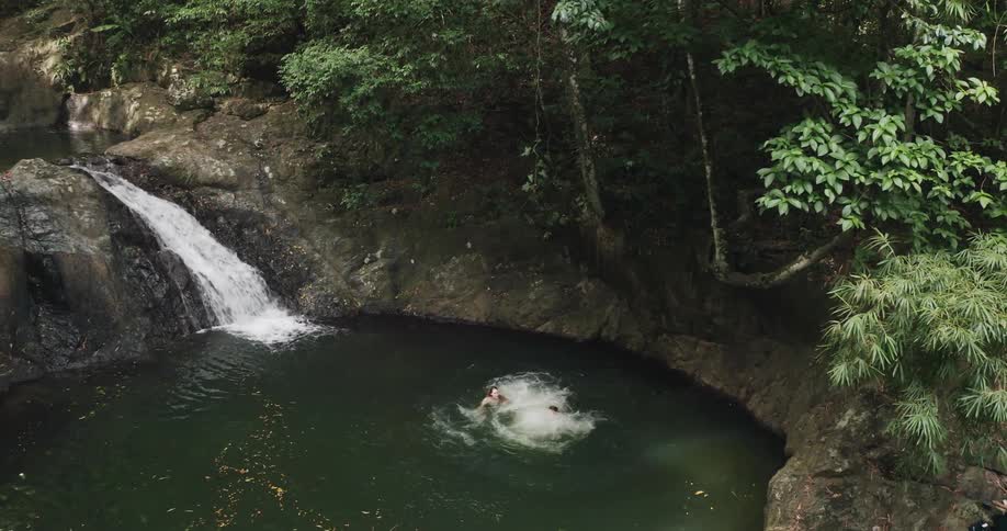 Couple jumping into a waterfall swimming hole