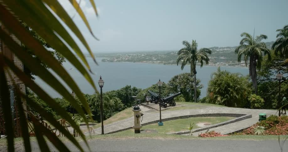 Two people walk around in a park with cannons placed near a shoreline