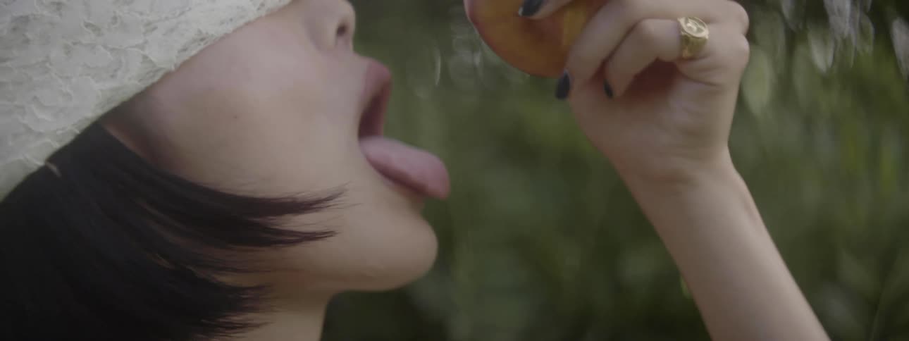 Woman wearing lace blindfold lifts fruit to mouth
