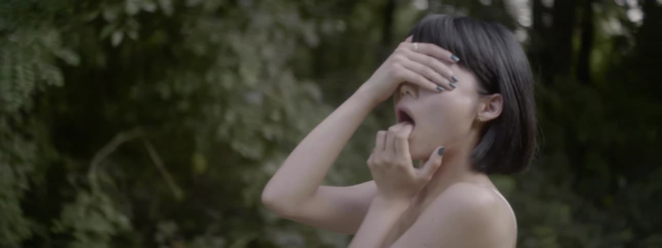 Woman standing outdoors covers her eyes with her hand