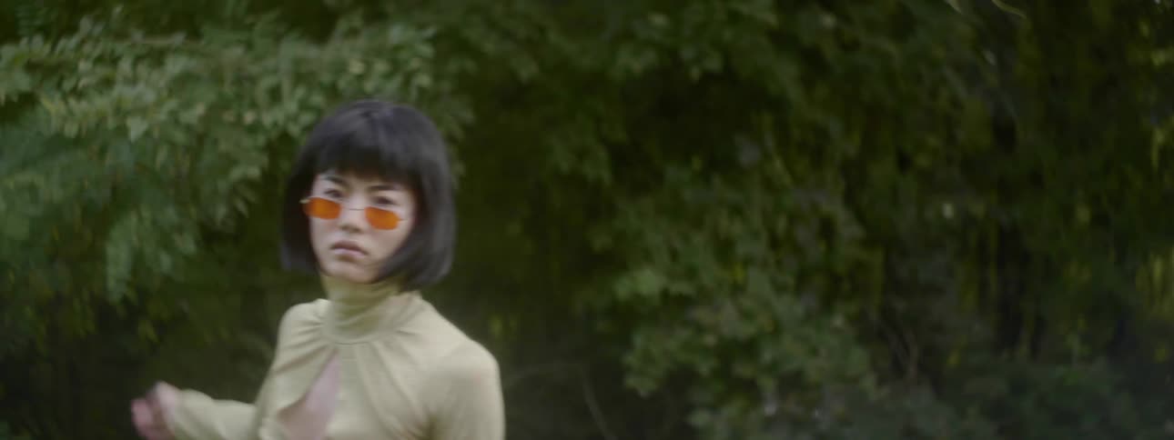An asian woman in a dress and sunglasses dances outdoors