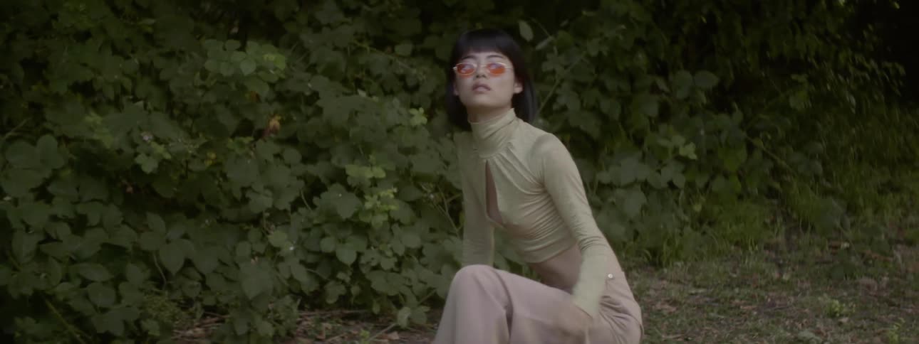 A woman with sunglasses squatting posing and dancing with plants in the background