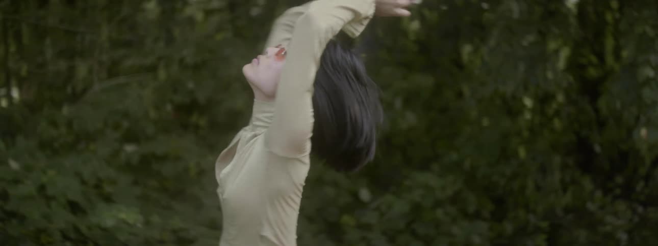 An asian woman spins outdoors with her arms up in the air
