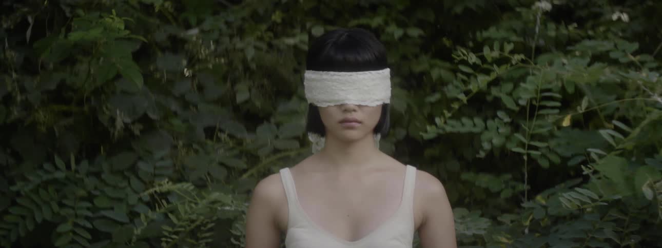 An asian woman wearing a blindfold stands outdoors
