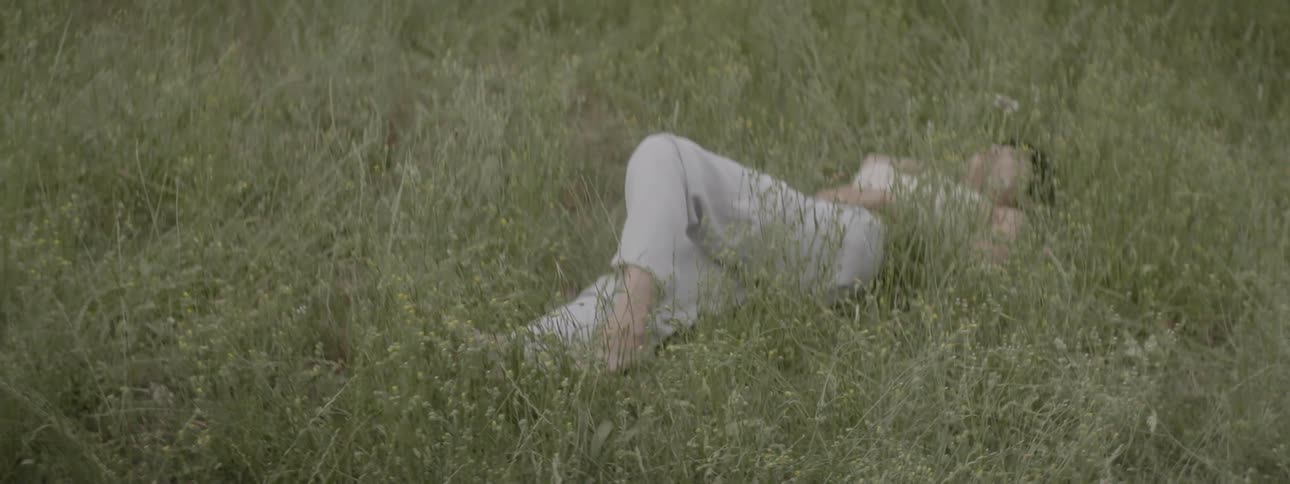 A white person lies on their back in a grassy area