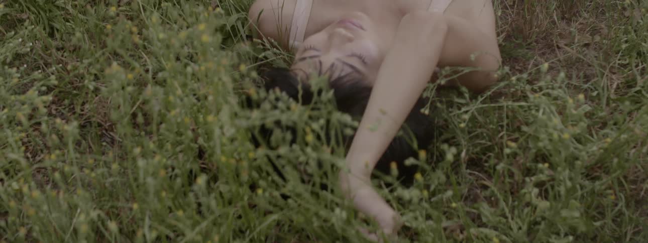 Woman wears sleeveless outfit reclining on back among wildflowers and grasses