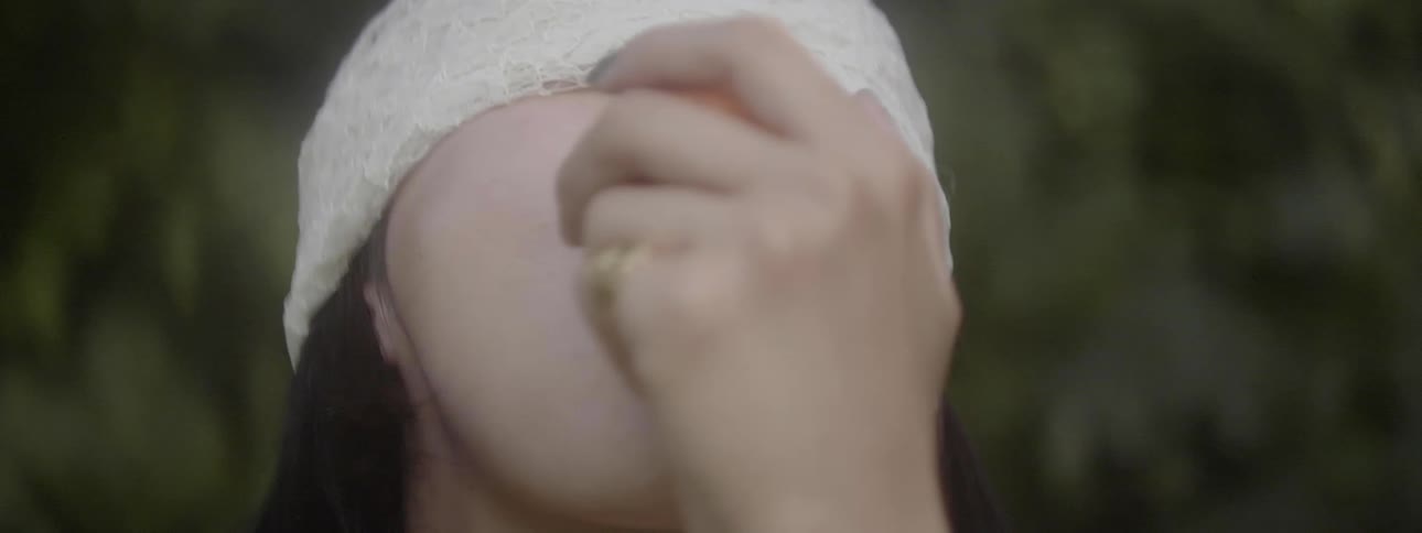 A blindfolded woman holds a peach to her mouth with her tongue extended