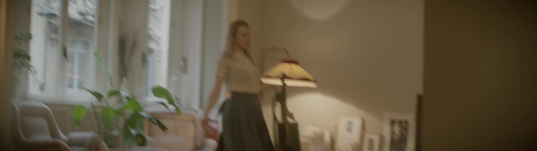 A woman dances while picking up her shoes and cleans a living room