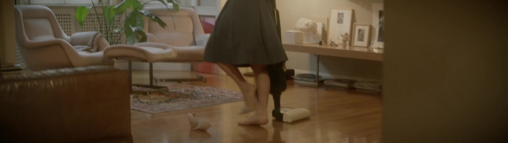 A young white woman in a dress does a sexy dance with a vacuum cleaner in an apartment living room