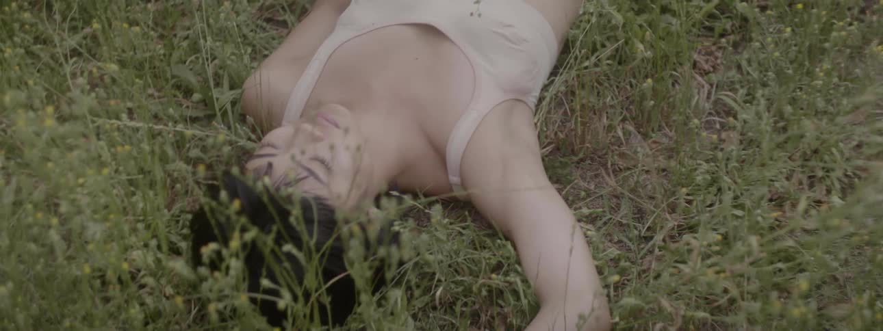 A young asian woman in undergarments lying in tall grass during the day